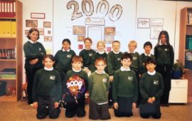 primary students posing for a group photo in the their classroom with 2000 written on the wall behind them