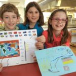three primary students displaying their work