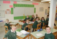 old photo of primary students sitting at their desks smiling for the camera